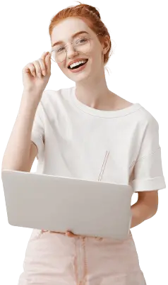 Image of a smiling, red haired woman standing with a laptop touching her glasses